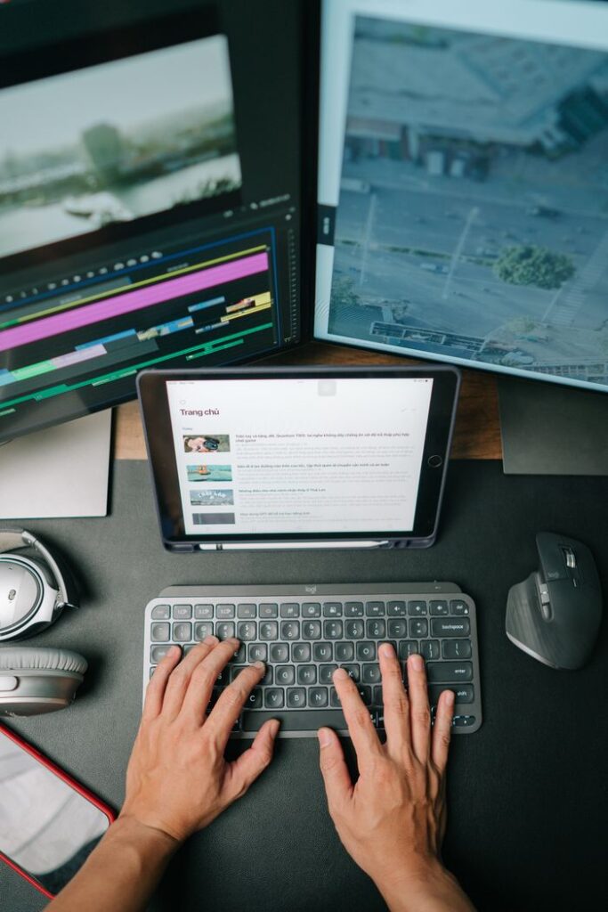 Person typing on keyboard in modern workspace with multiple screens displaying content.