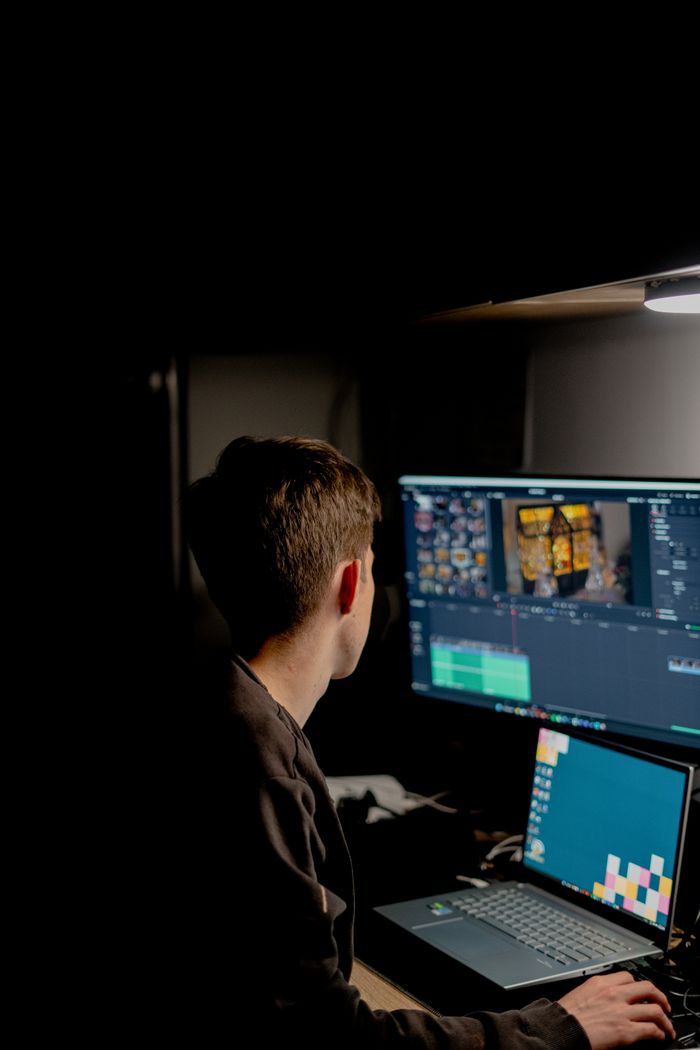 A creative professional editing video content on dual screens in a dark room.