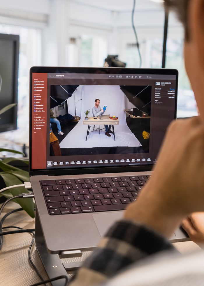 A man using a laptop for photo editing in a bright, modern workspace with a photography setup.