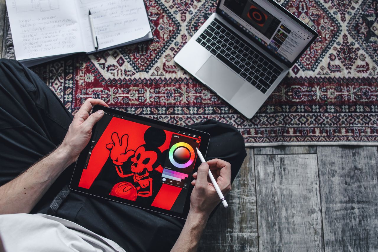 Projects A person drawing on a digital tablet while seated on a patterned rug indoors.