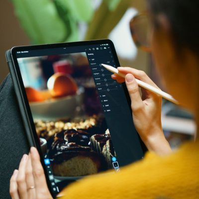 A woman uses a stylus to edit photos on a tablet, showcasing freelance creativity.
